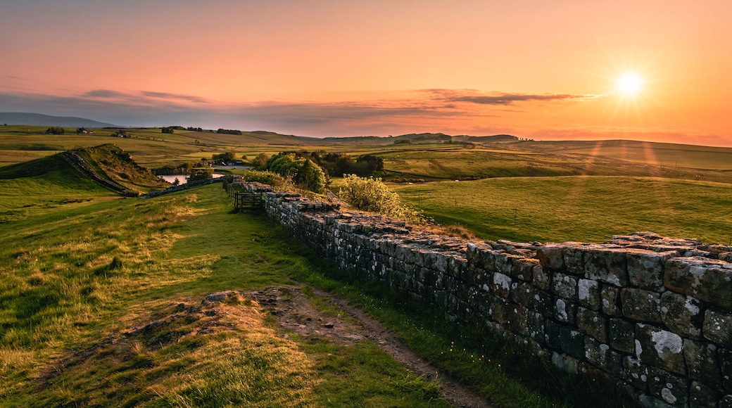 Eine Steinsicht, ein grünes Feld und ein Sonnenuntergang über sanften Hügeln.