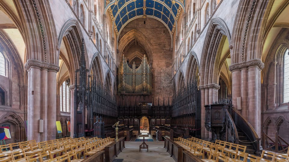 A cathedral interior with a high vaulted ceiling, arched windows, and rows of wooden pews.