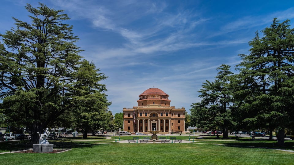 A large red-brick building with a dome, surrounded by green grass and trees.
