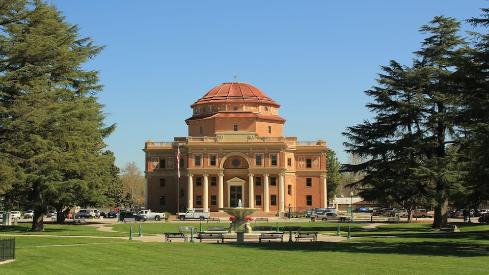 A large brick building with a dome and columns, surrounded by green grass and trees.