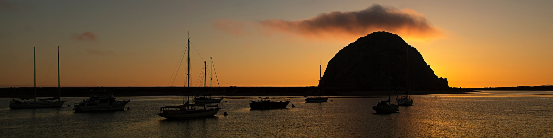 A sunset over a body of water with several boats and a prominent hill in the background.