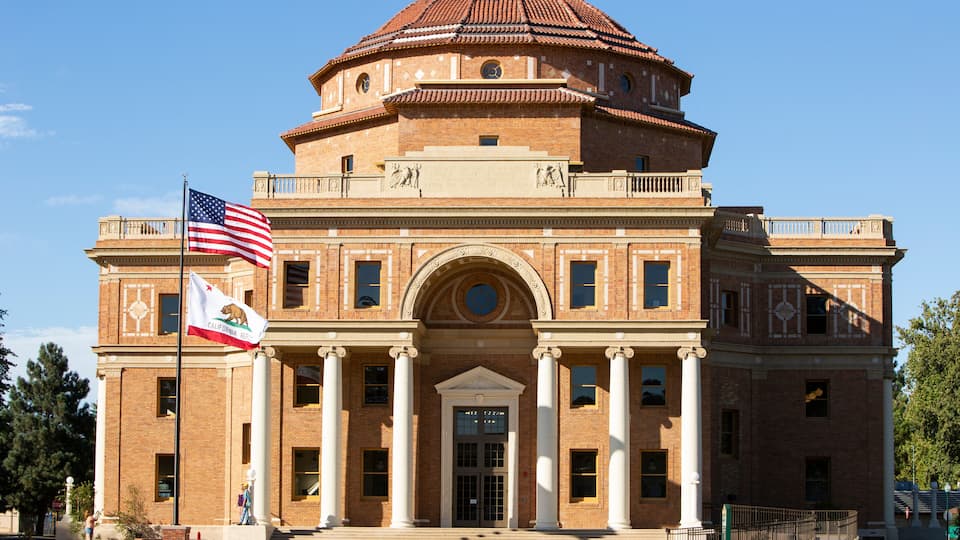 A large brick building with a dome, columns, and flags.