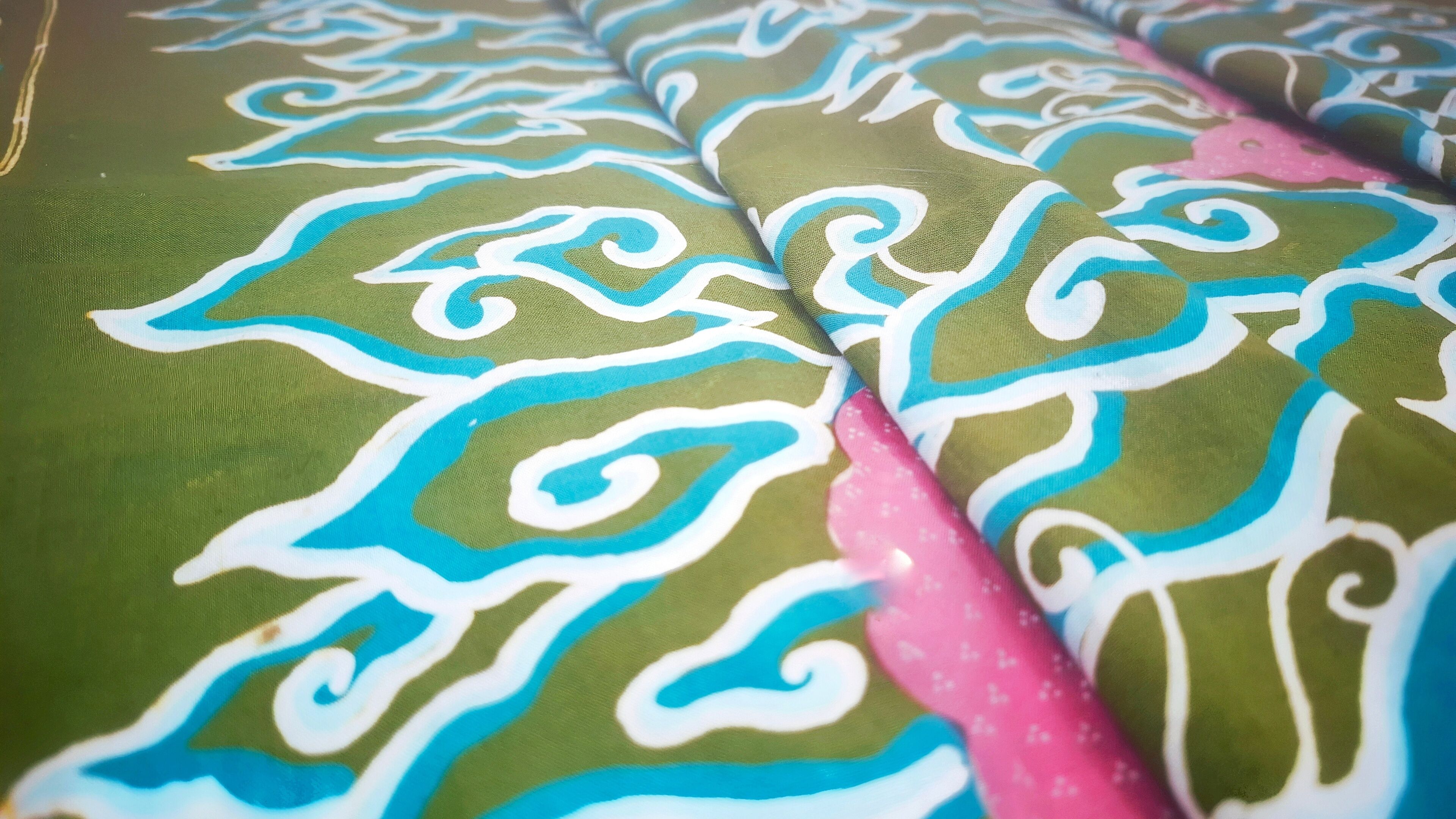 A fabric with a green background and blue and white swirling patterns.