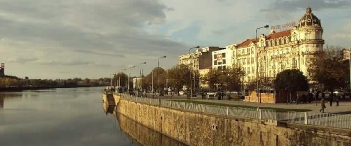 Ein Fluss mit einer Steinbrücke, ein großes historisches Gebäude mit Kuppel und ein klarer Himmel.