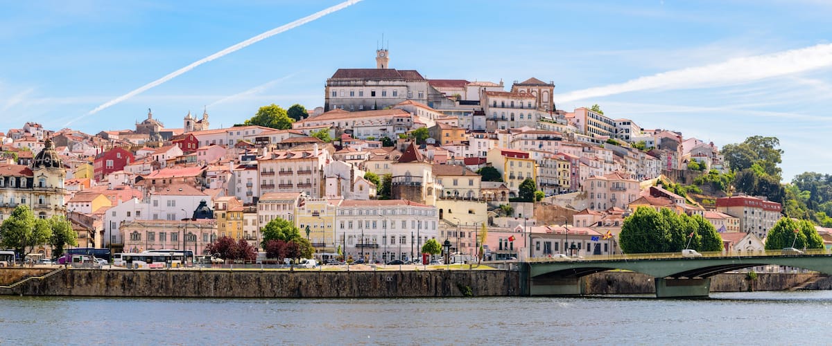 A historic cityscape with a prominent hilltop church, a bridge over a river, and a dense urban area with colorful buildings.