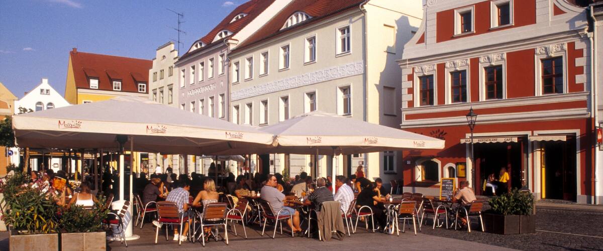 A bustling outdoor café with patrons seated at tables under large umbrellas.