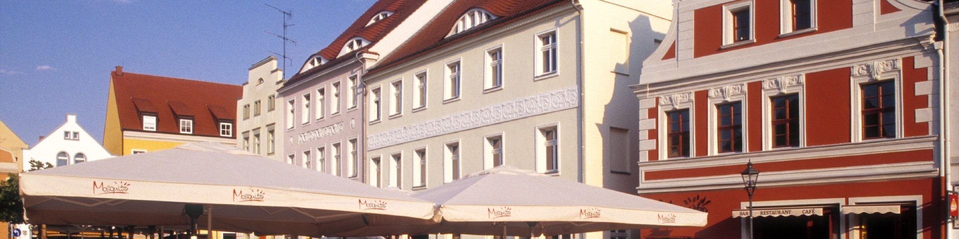 A bustling outdoor café with patrons seated at tables under large umbrellas.