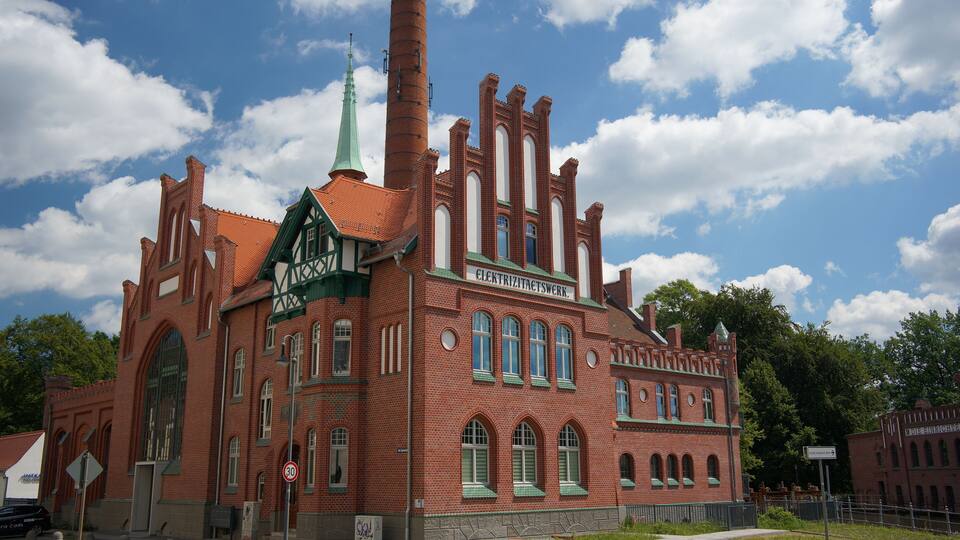 A historic red brick building with green accents and a tall chimney.