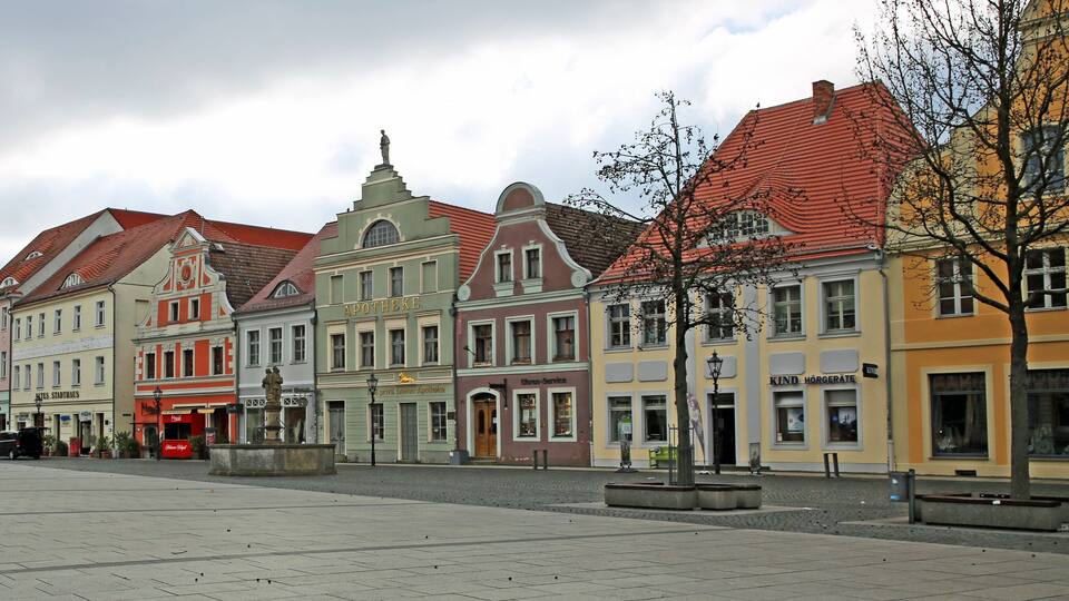 A historic European square with colorful buildings, a statue, and a cobblestone plaza.