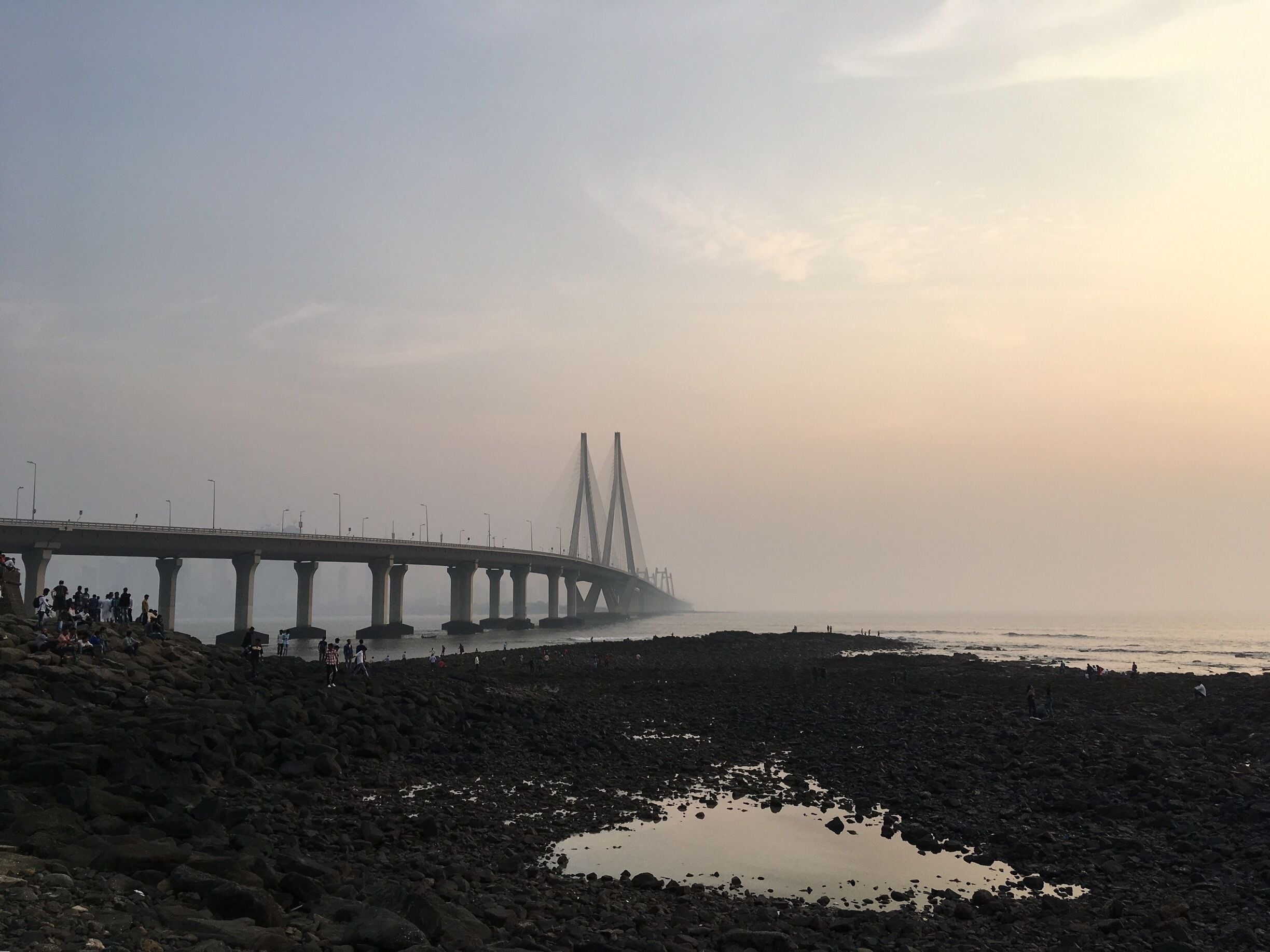 A bridge over a rocky beach with people walking along the shore.