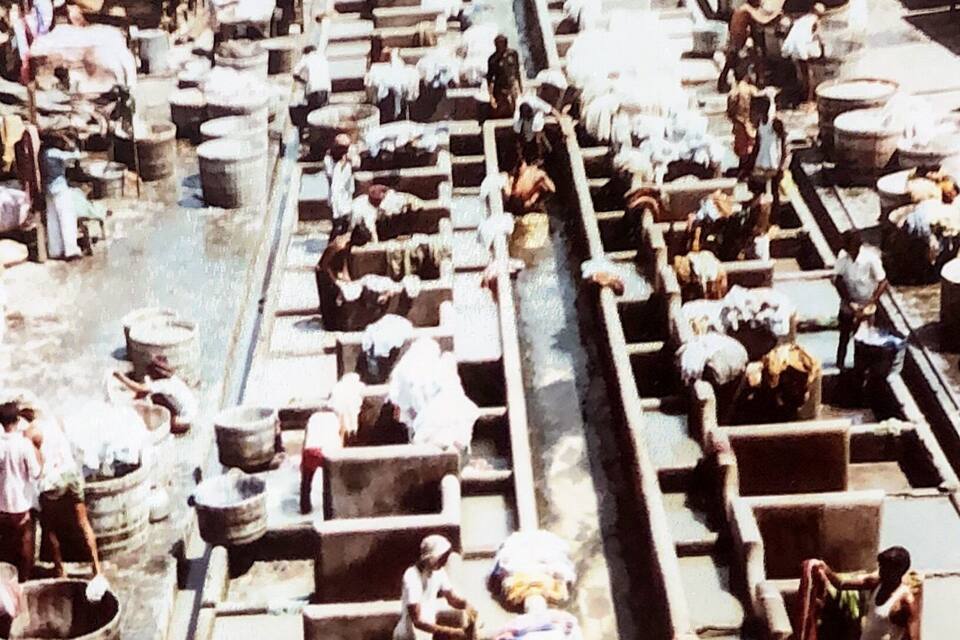 A crowded outdoor laundry facility with rows of tubs and workers.