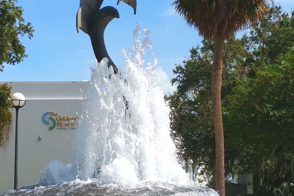 A dolphin sculpture leaping out of a fountain with water splashing around it.