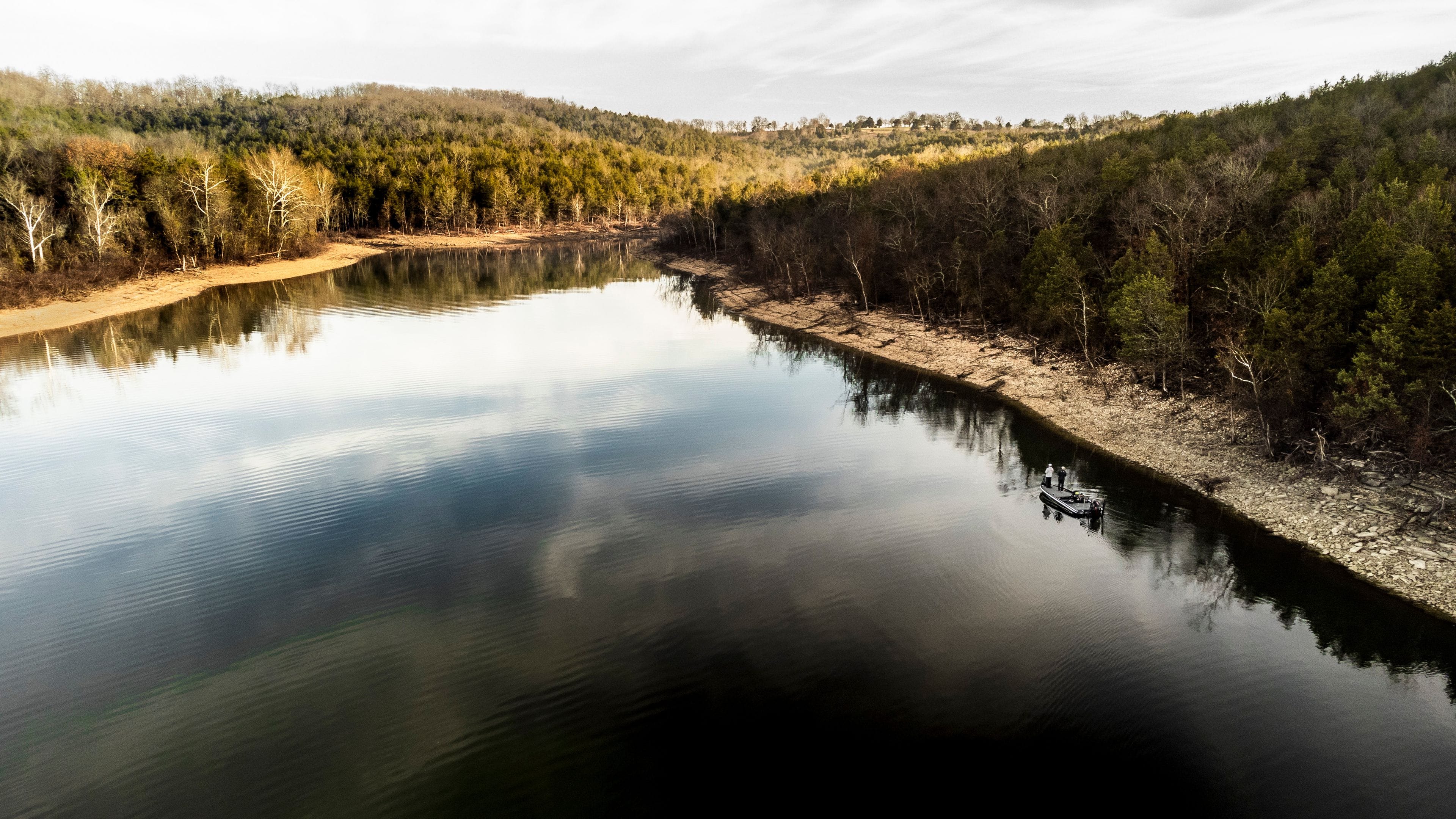 A calm river surrounded by dense forest and hills.