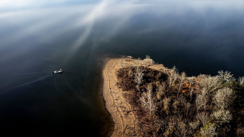 A boat on a calm lake, a rocky shoreline, and sparse vegetation.