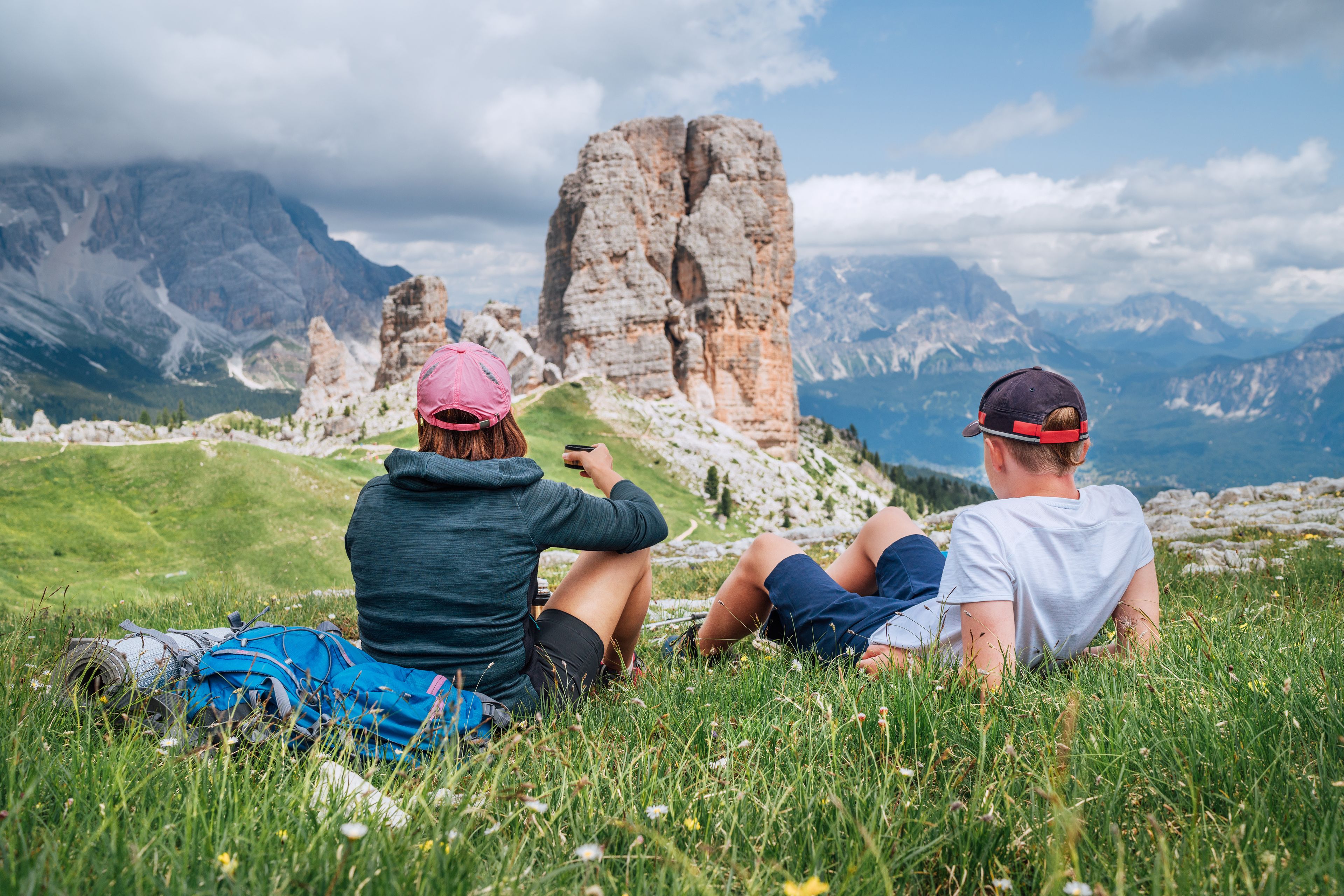 Mother and son backpackers have a tea brake on a green mountain hill with the picturesque Dolomite Alps Cinque Torri formation, Nothern Italy. Family values, active people and mountains concept.
