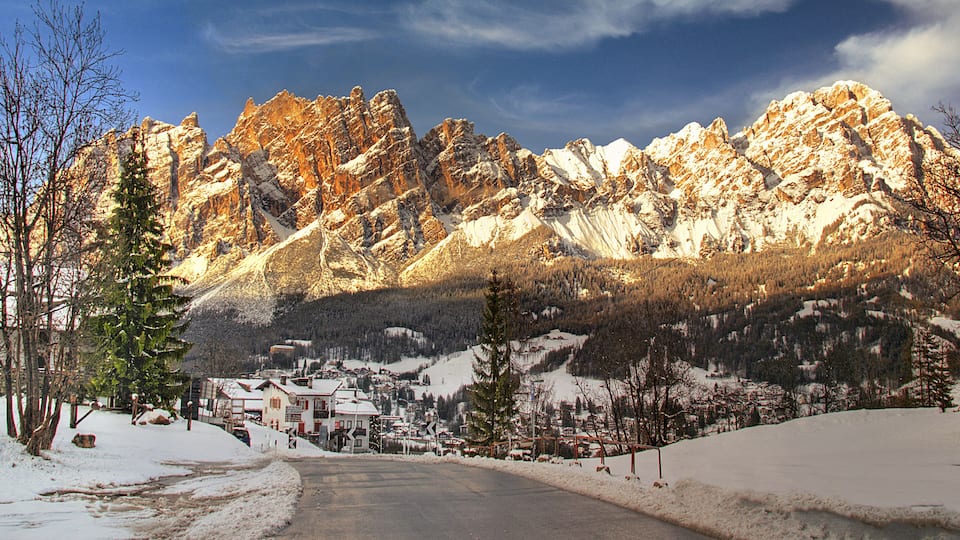 A snow-covered mountain road leading to a small village with houses and trees.