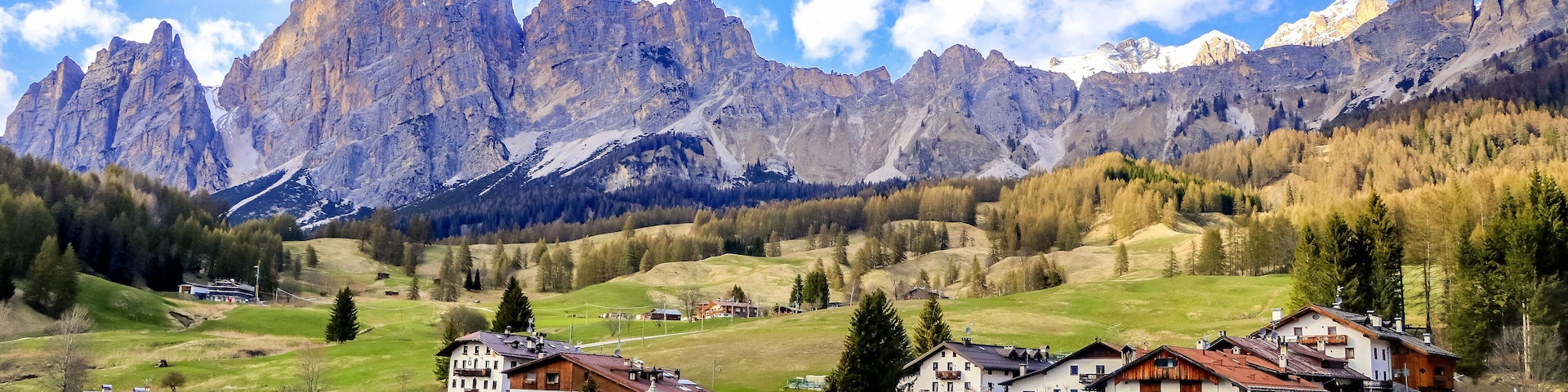 A mountain village with traditional houses, a road, and a valley with trees and mountains in the background.