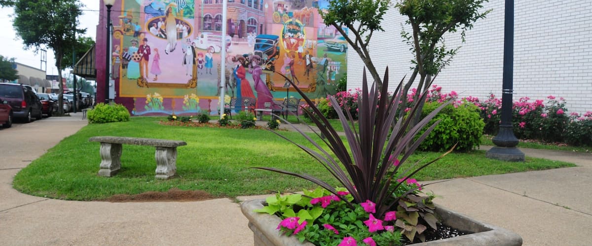 A mural on a building, a bench, and a planter with flowers.