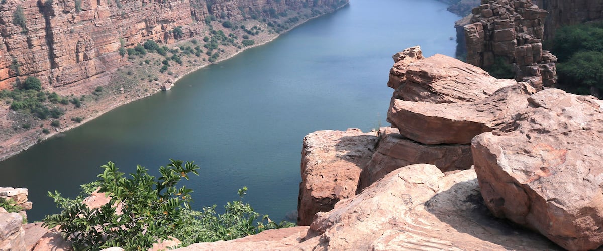 A canyon with a river, rocky cliffs, and sparse vegetation.