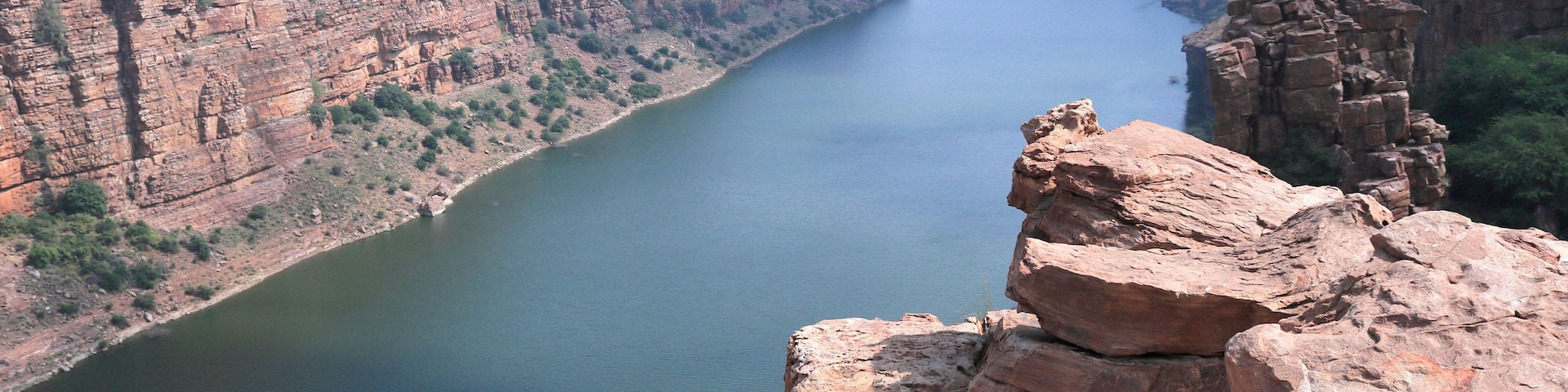 A canyon with a river, rocky cliffs, and sparse vegetation.