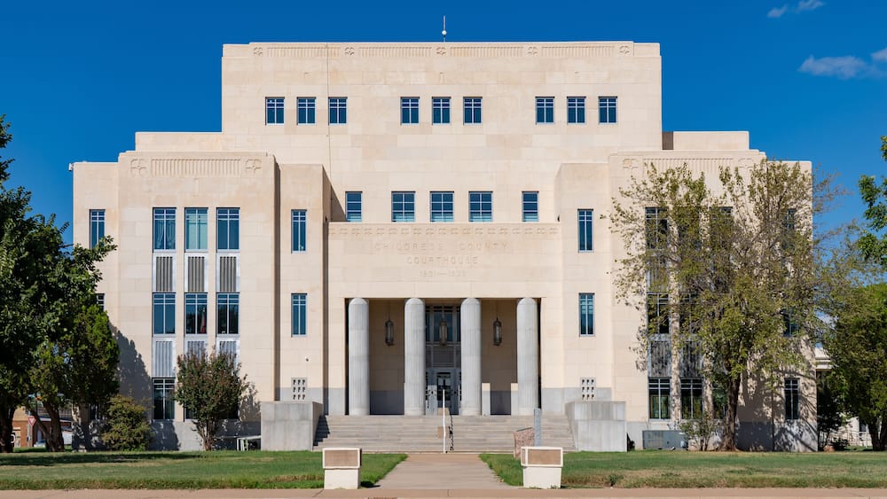 Un grand bâtiment beige abritant le tribunal, avec une entrée centrale flanquée de colonnes, entouré d’une pelouse bien entretenue et d’arbres.