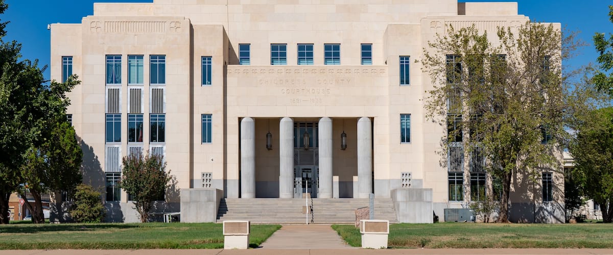 A large, beige courthouse with a central entrance flanked by columns, surrounded by a well-maintained lawn and trees.