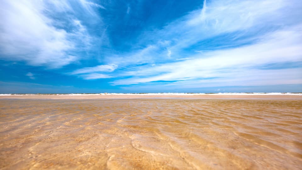 A beach with clear water and a blue sky with clouds.