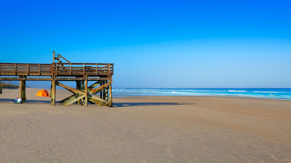 A wooden pier extending into a sandy beach with the ocean in the background.