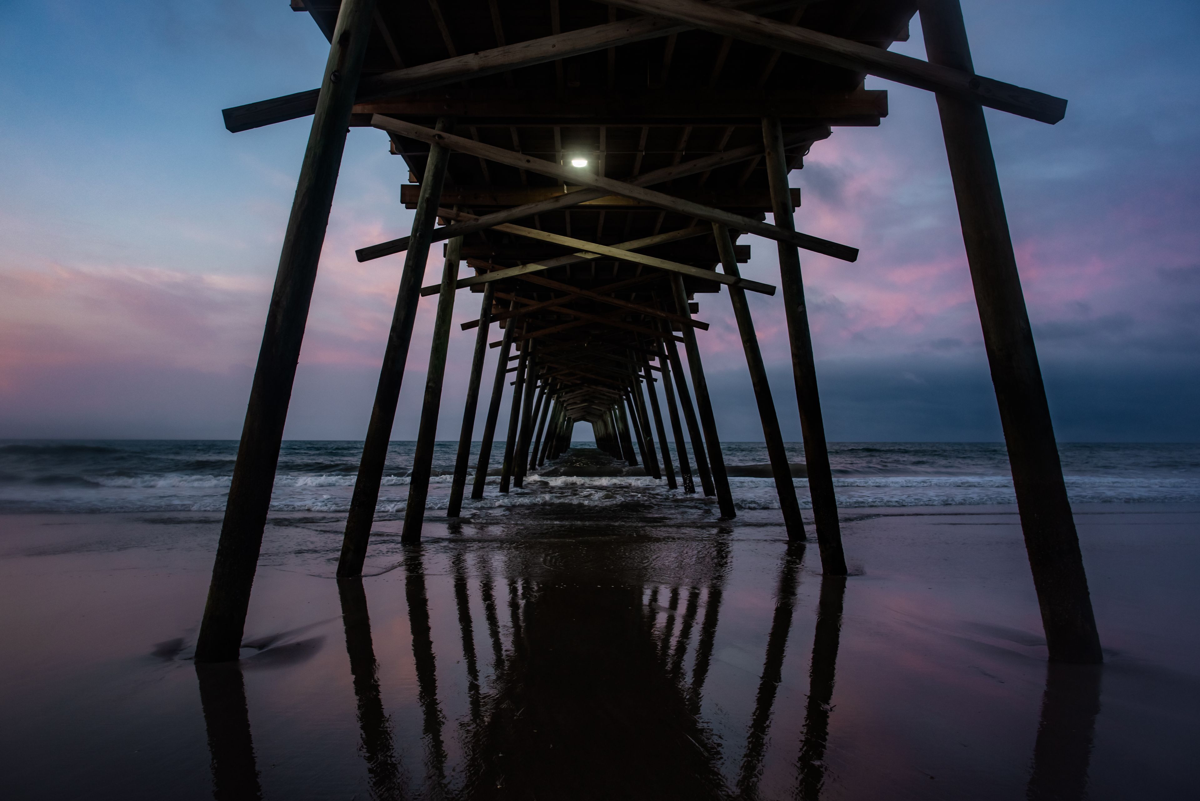 A wooden pier extending into the ocean at dusk with a clear sky above.