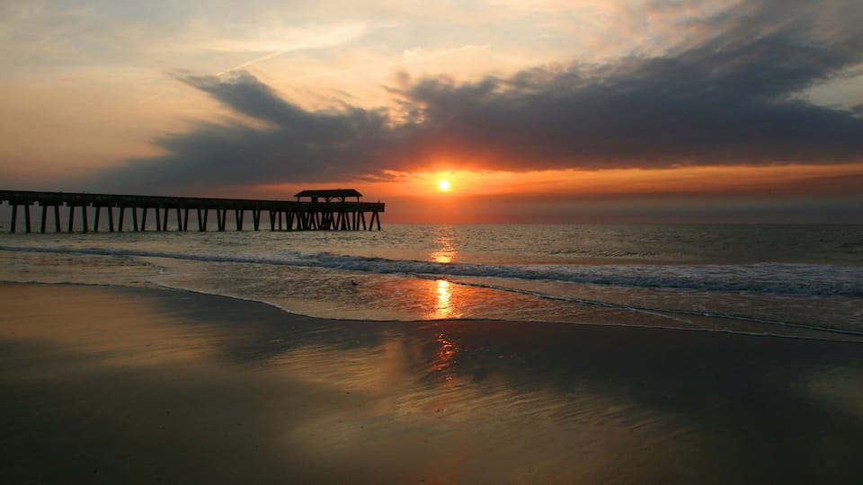 A sunset over the ocean with a pier extending into the water.