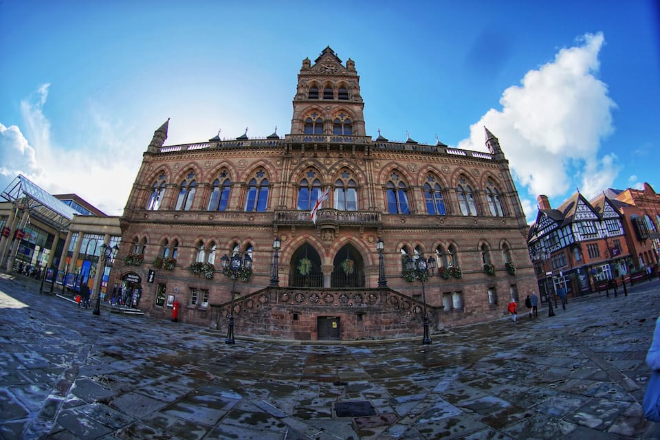 A historic building with intricate architecture, a prominent clock tower, and a cobblestone plaza.