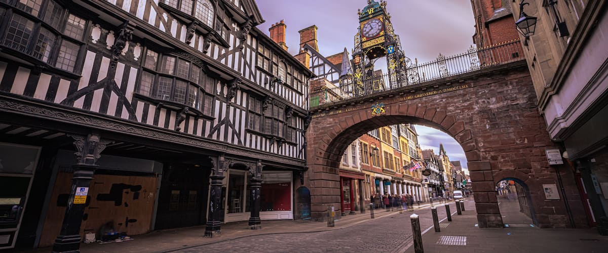 A historic street with a half-timbered building, a clock tower, and an archway.
