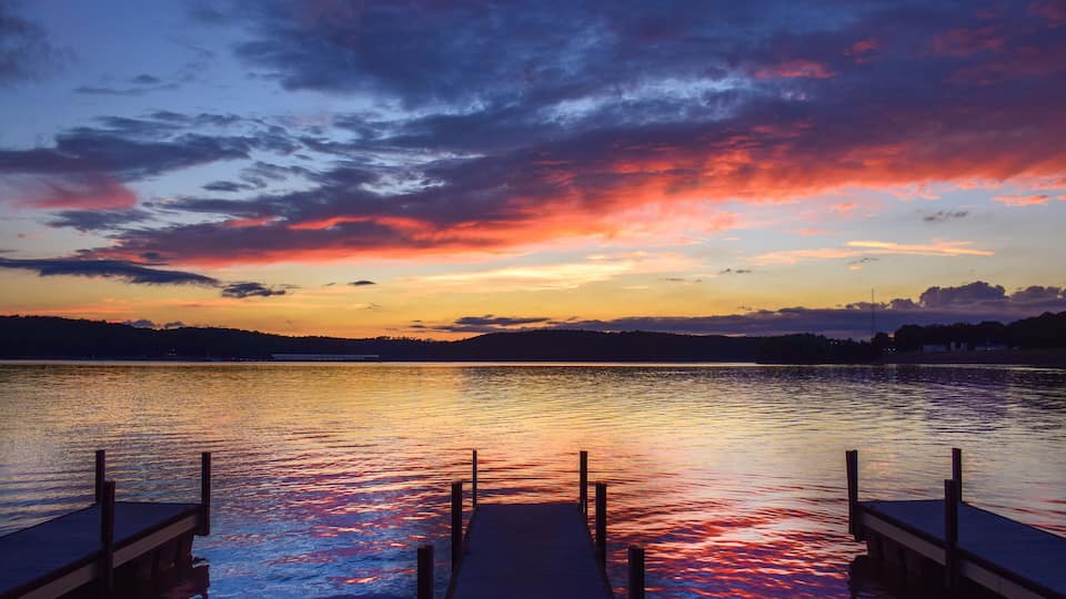 A sunset over a calm lake with a wooden dock extending into the water.