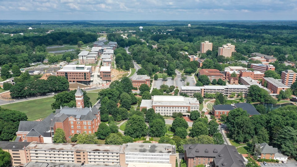 An aerial view of a university campus with multiple buildings, green spaces, and a prominent clock tower.
