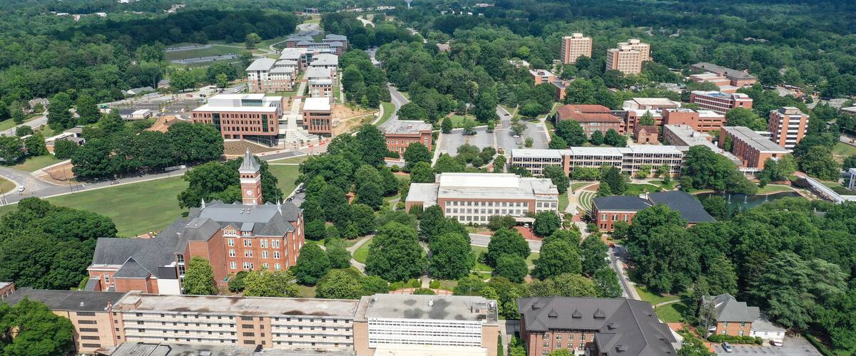 An aerial view of a university campus with multiple buildings, green spaces, and a prominent clock tower.