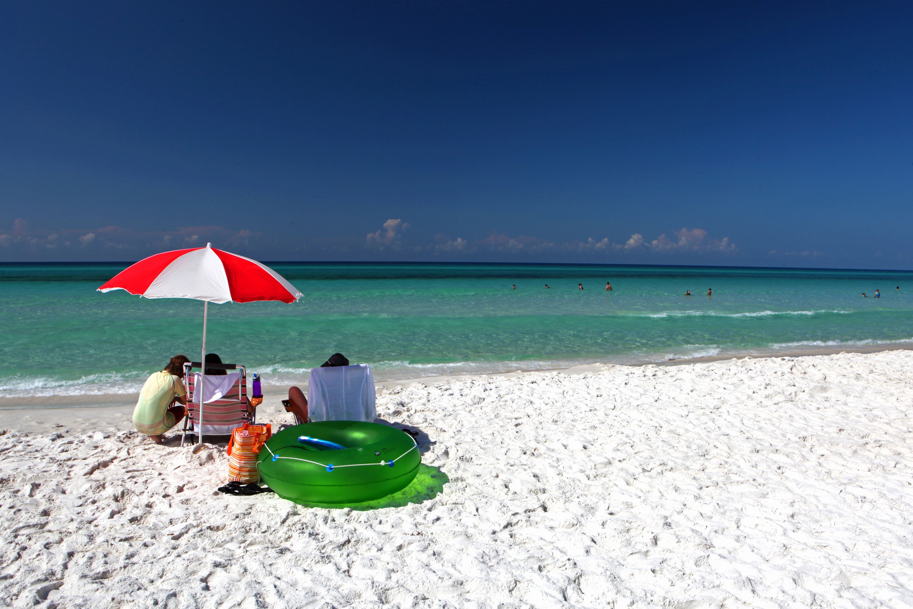 A family sits under an umbrella on a sandy beach in the Florida panhandle.