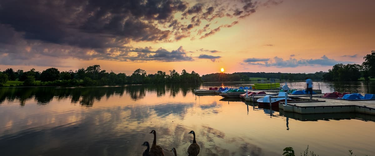 Panorama of Jacobson Park lake in Lexington, Kentucky during early morning sunrise. Marina with paddle boats and kayaks in the right side of the image, reflections of the trees and clouds on the left