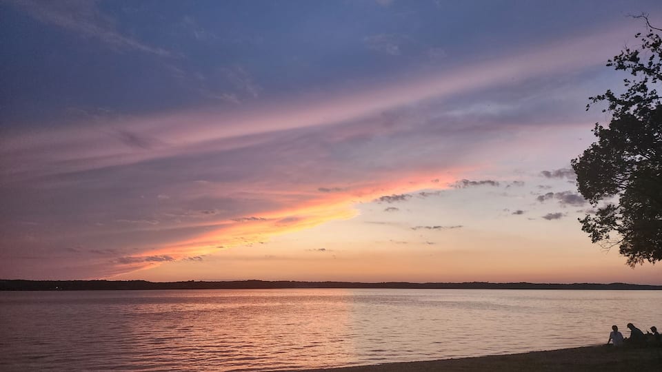 A sunset over a calm lake with silhouettes of people on the shore.