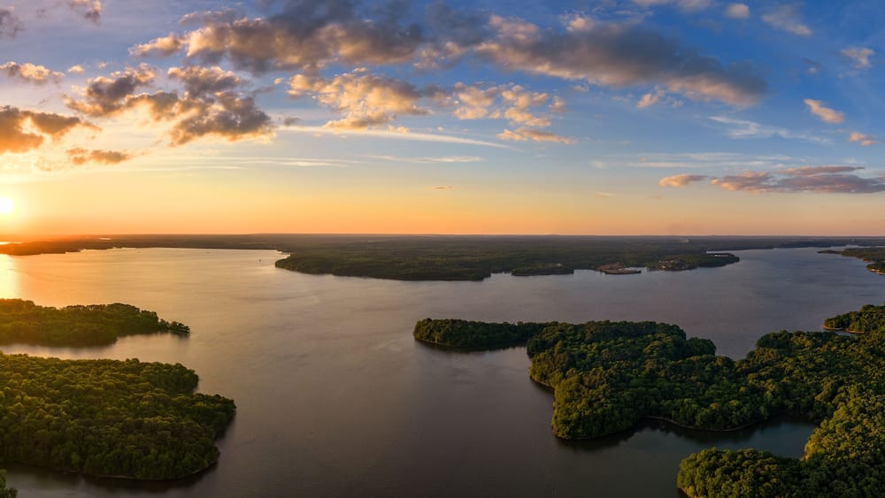 A sunset over a calm lake with several islands surrounded by dense forest.