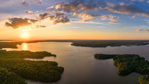 A sunset over a calm lake with several islands surrounded by dense forest.