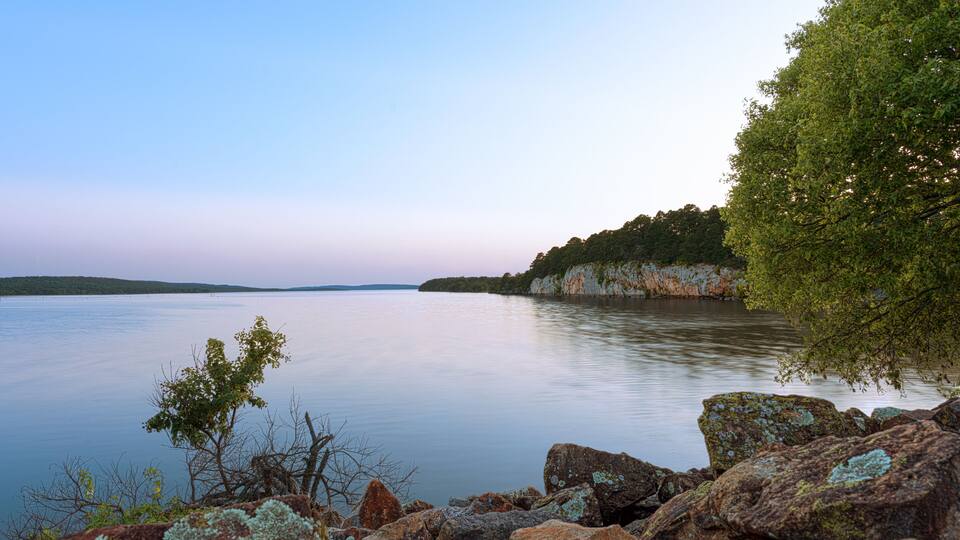 A calm lake with rocky shores and a forested cliff.