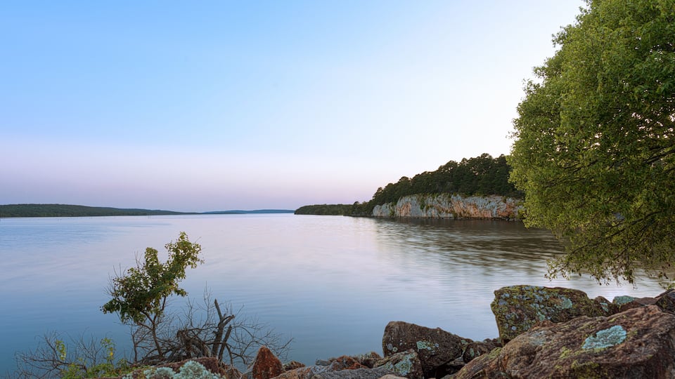 A calm lake with rocky shores and a forested cliff.