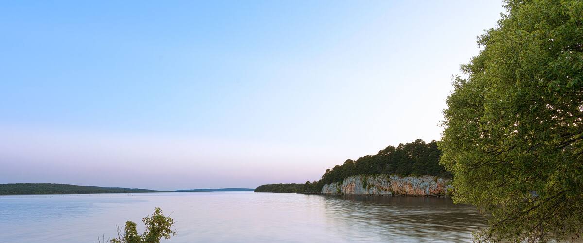 A calm lake with rocky shores and a forested cliff.