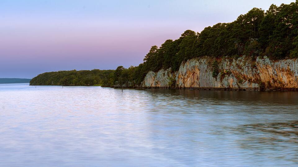 A calm lake with a rocky cliff covered in trees.