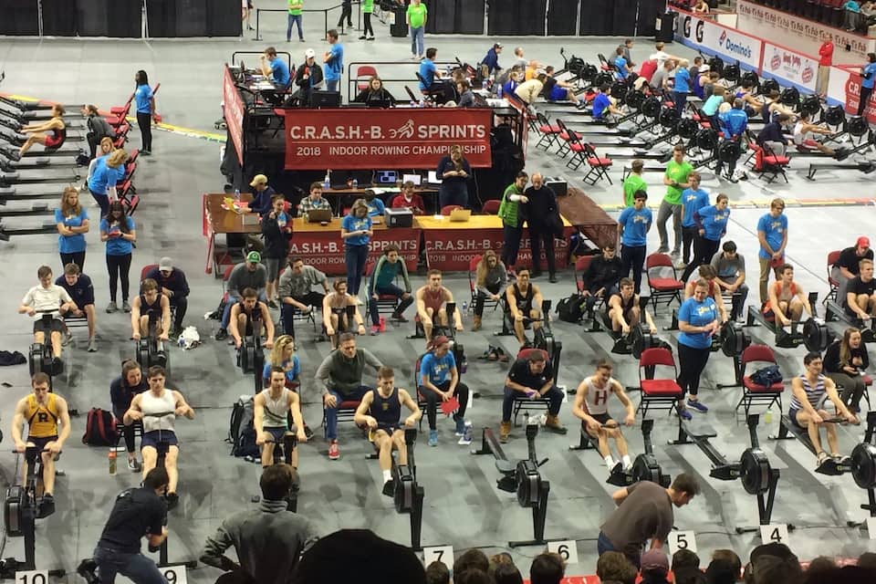 Una competició de rem interior amb esportistes en ergòmetres, jutges i espectadors.