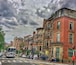 A busy urban street with classic red brick buildings, a bus, and pedestrians crossing.