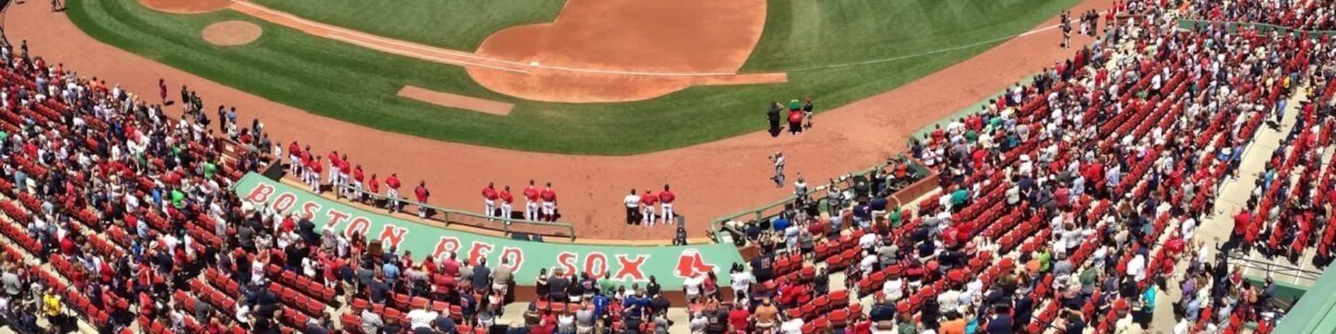 A baseball stadium with a large American flag, a crowd of spectators, and the Boston Red Sox logo.