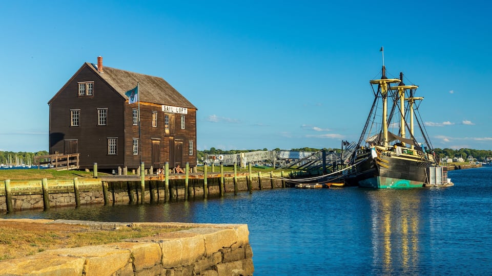 A historic sail loft building and a large sailing ship docked at a harbor.