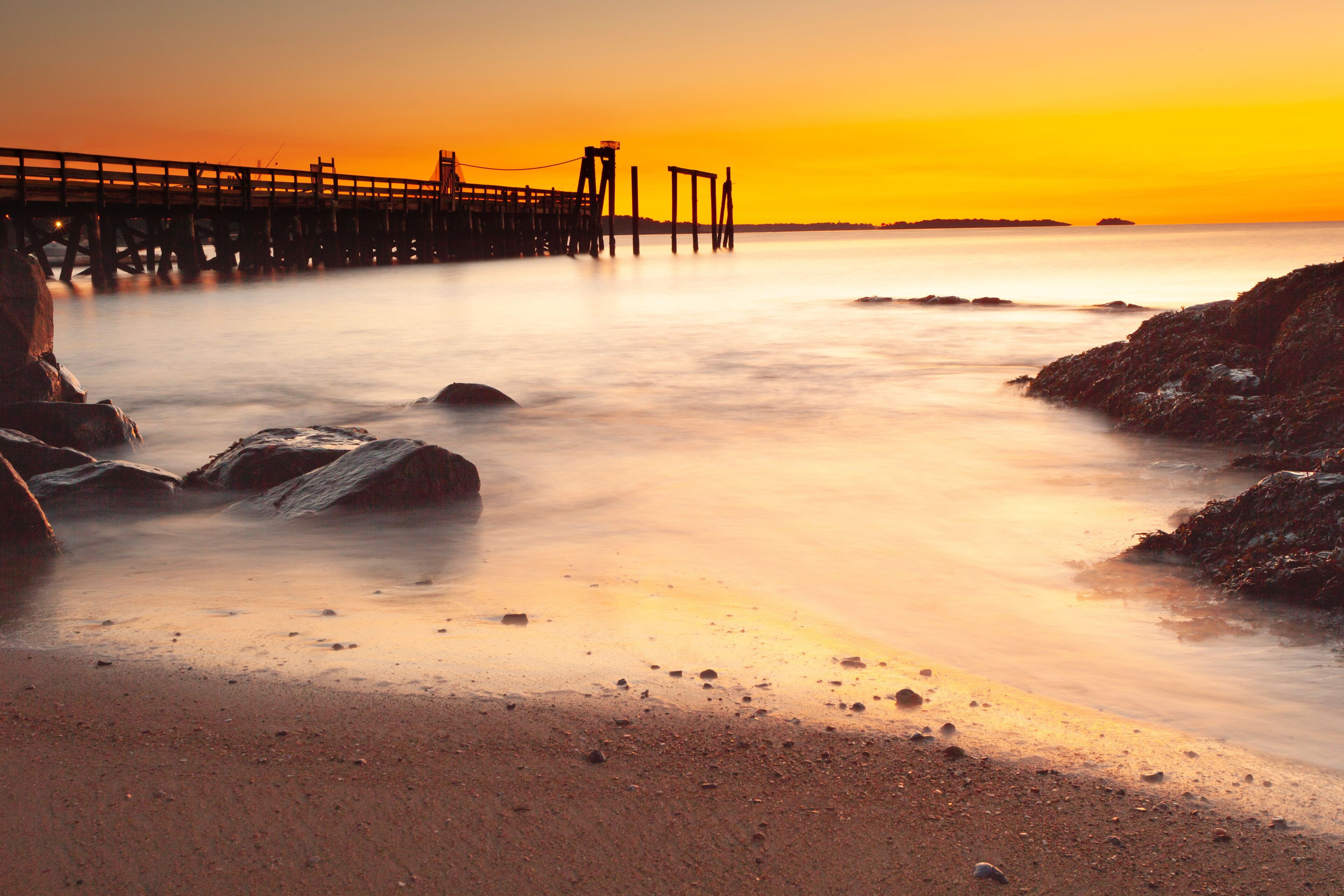 Un atardecer sobre una playa con un muelle que se adentra en el agua.