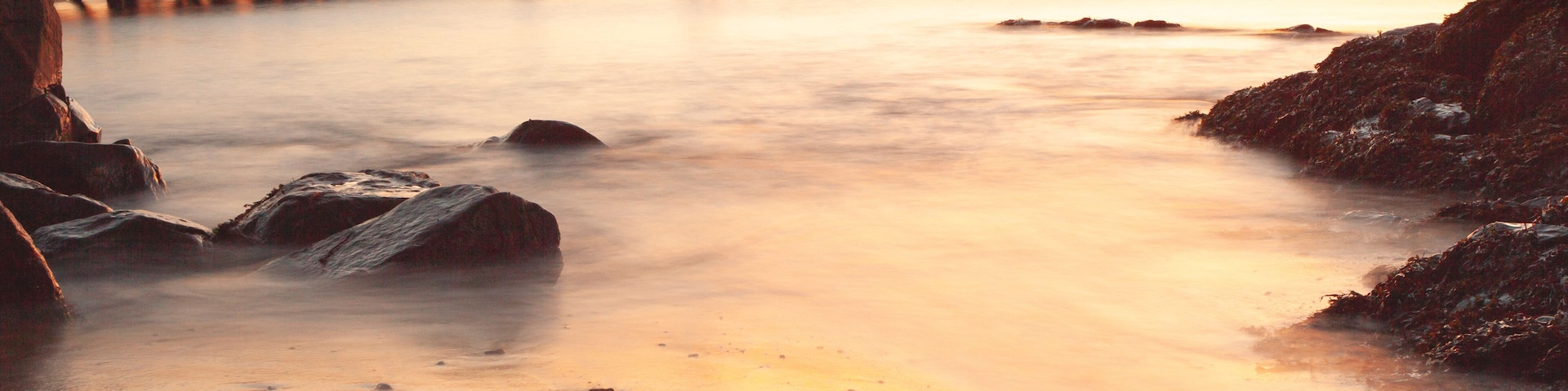 Un atardecer sobre una playa con un muelle que se adentra en el agua.